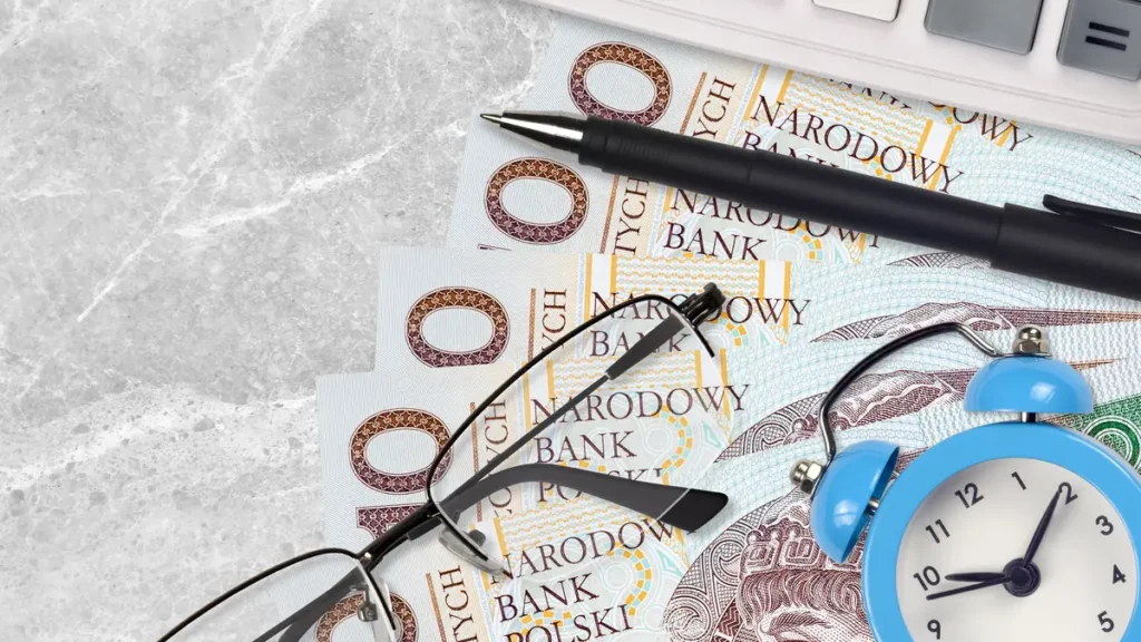 Banknoty 100 zł, kalkulator, okulary i budzik - liczenie odsetek z lokaty na 3, 6 i 12 miesięcy
