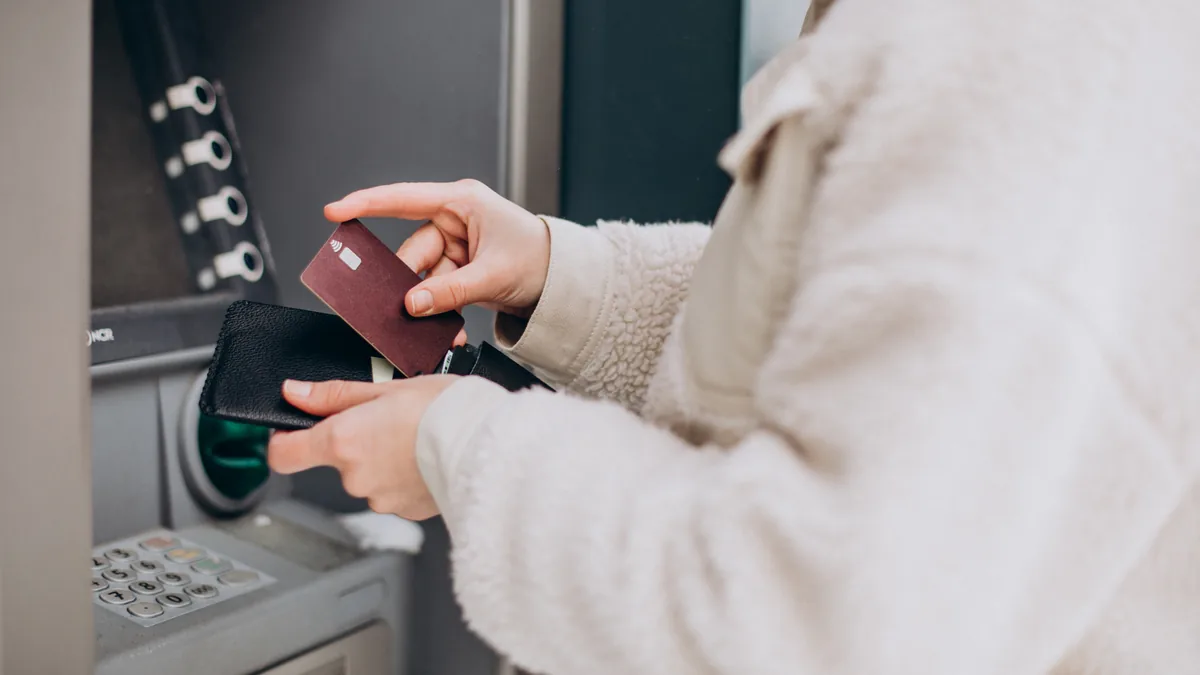 Kobieta wyjmuje kartę z portfela przy bankomacie przed wypłatą gotówki z konta studenckiego