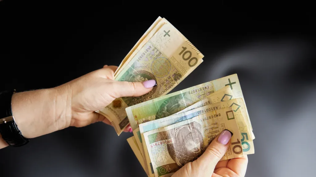 Kobieta przelicza banknoty 100, 50 i 10 zł - wypłata netto przy płacy minimalnej w 2027 r.
