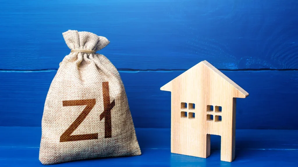 Worek z symbolem zł obok drewnianego domku - ile kredytu hipotecznego bank pożyczy przy danych zarobkach